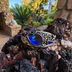 Midnight Ember sterling silver cuff featuring three Boulder opals with blue and green flashes, photographed on dark textured wood.

