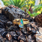  Solar Crest gold opal ring resting on dark rock, with blue and green color visible.
