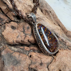 Ocean Relic Australian Boulder Opal pendant displayed on weathered driftwood showing engraved sterling silver details.