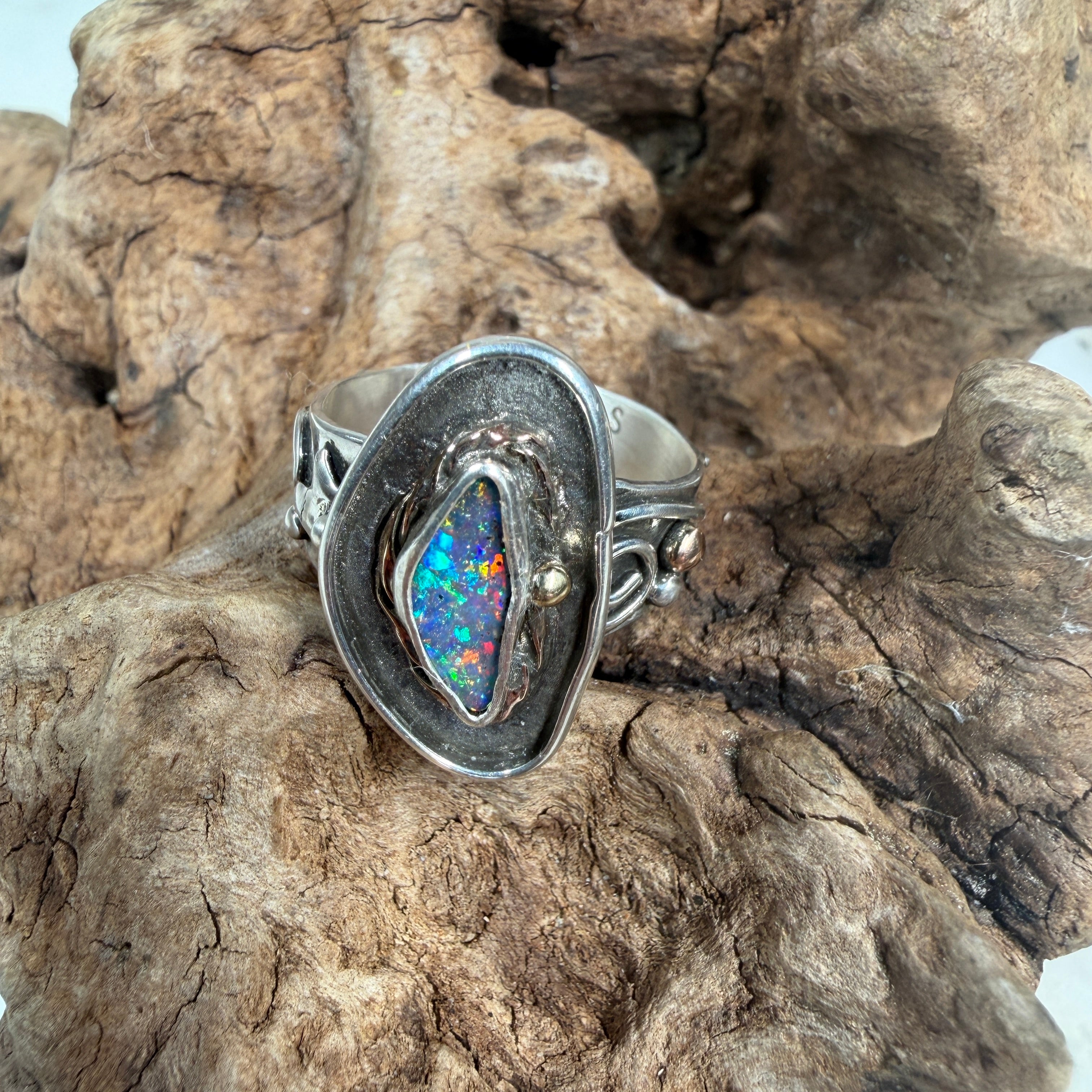 Reef Current handcrafted Australian Boulder Opal ring in .925 sterling silver with a 14K gold rope bezel and gold accents displayed on weathered driftwood.