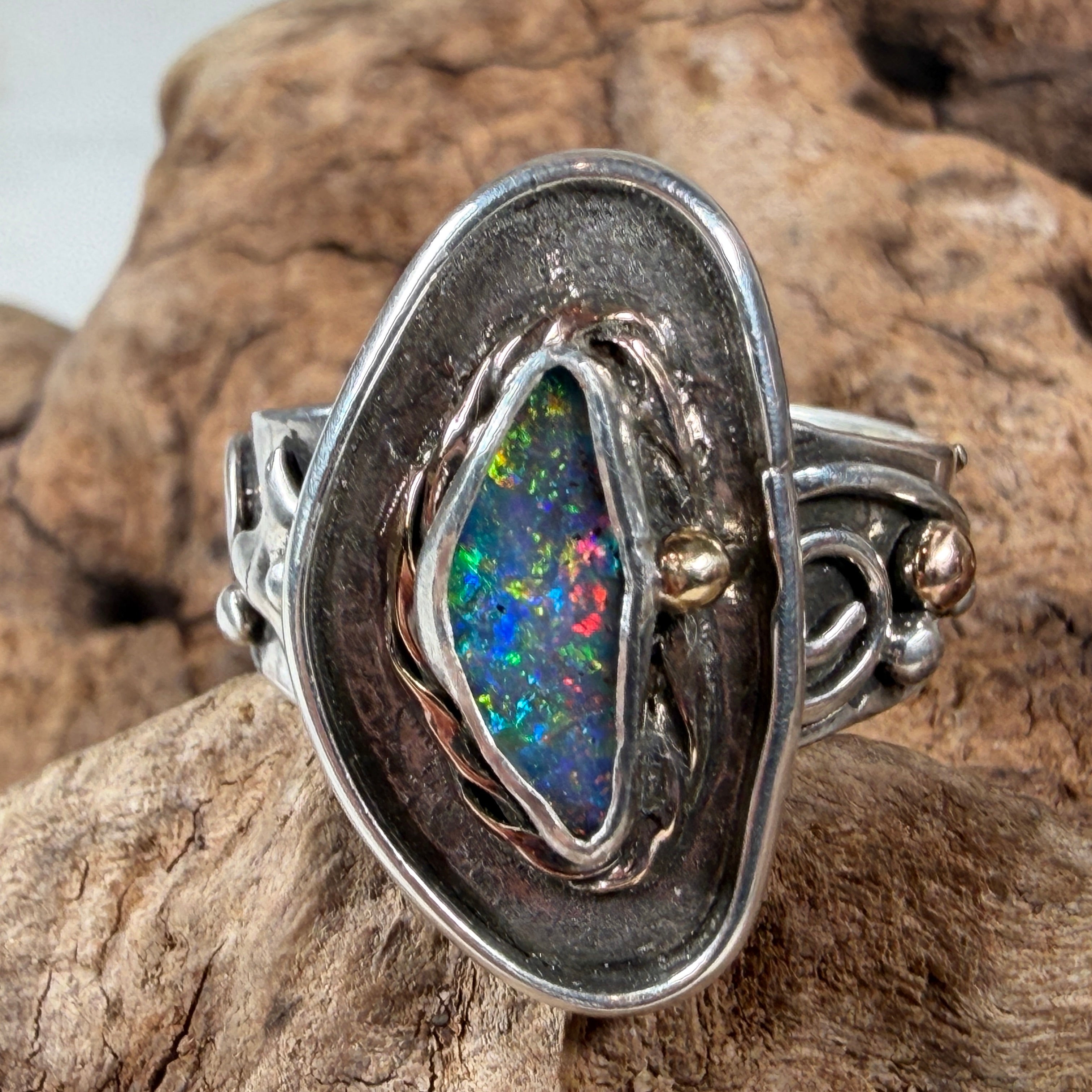 Reef Current handcrafted Australian Boulder Opal ring in .925 sterling silver with a 14K gold rope bezel and gold accents displayed on weathered driftwood.
