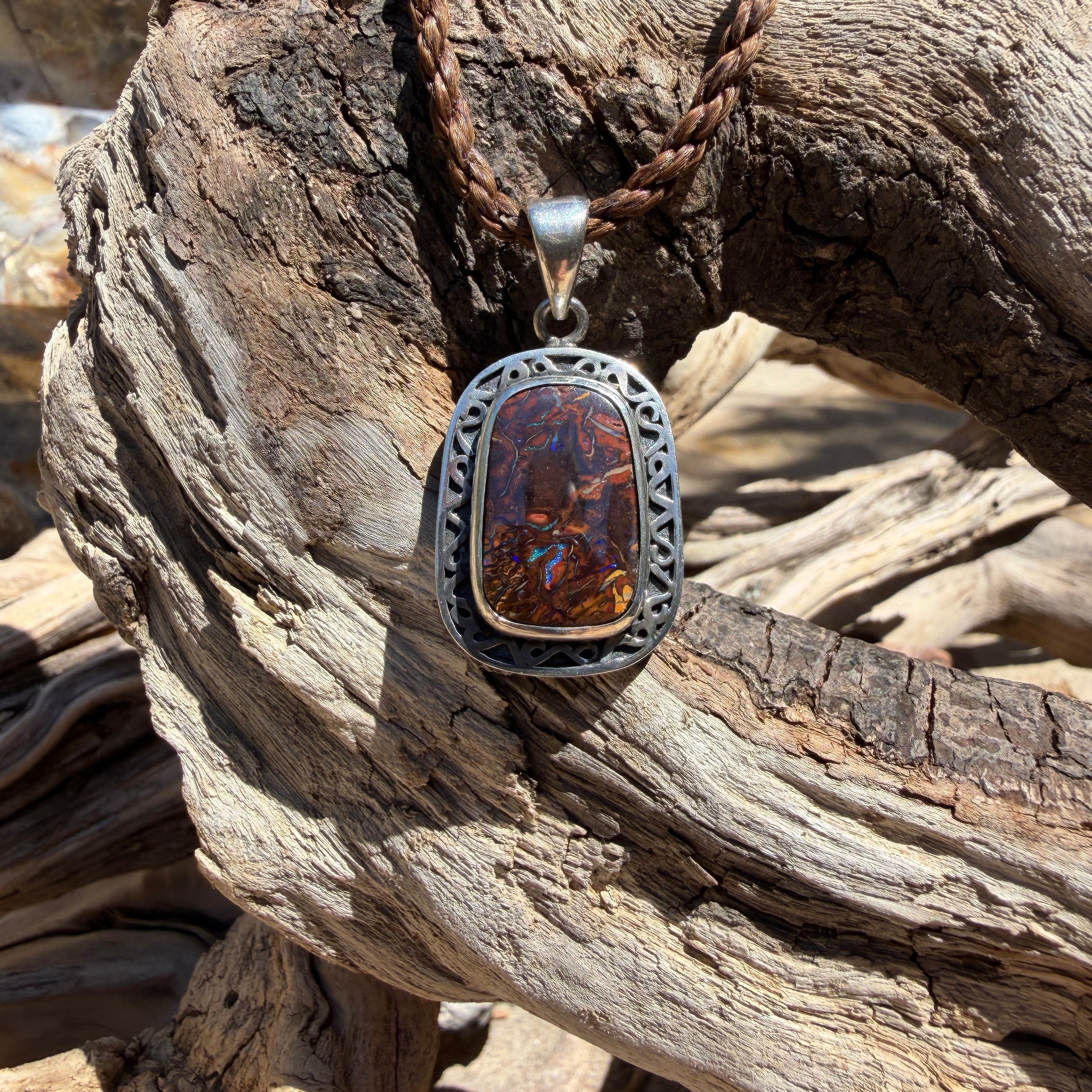 Discover Coastal Relic, a one-of-a-kind Australian boulder opal pendant handcrafted in sterling silver. Intricate engraved openwork details surround a natural 20 × 13 mm boulder opal with brilliant blue flashes.