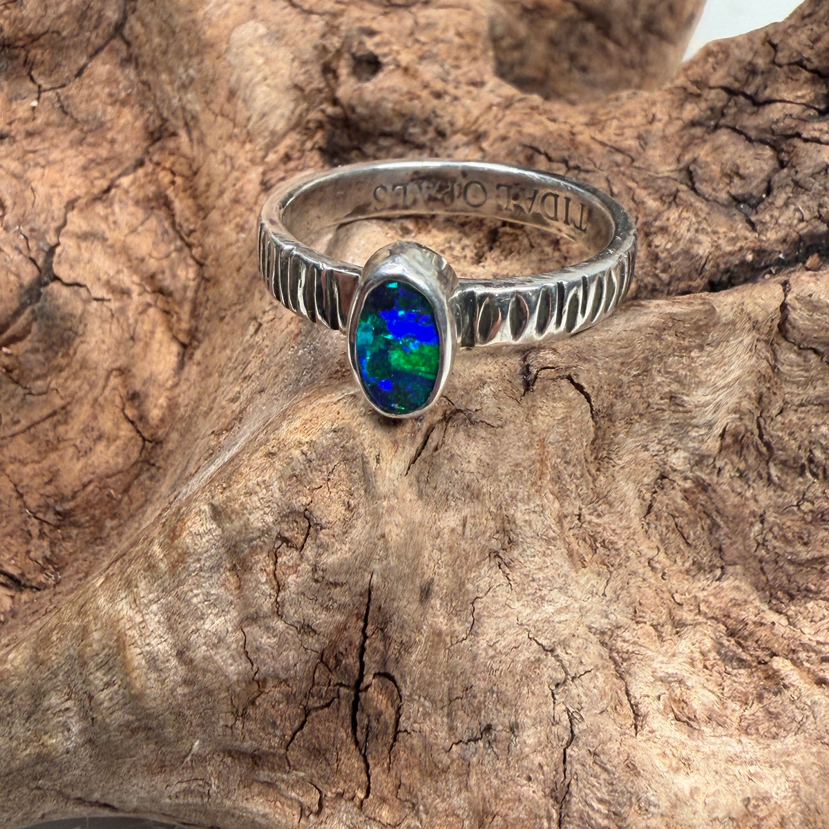 Handmade opal ring with intense green and teal color play in a polished silver setting.