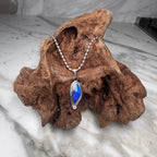Jewelry with a blue pendant on a piece of wood against a marble background
